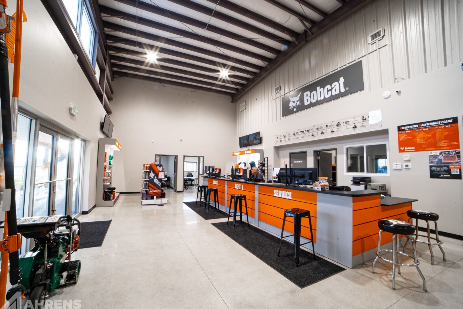 Bobcat of the Treasure Coast interior showroom — floor-to-ceiling ESWindows glass entry on left wall, Bobcat signage, service counter with orange branding