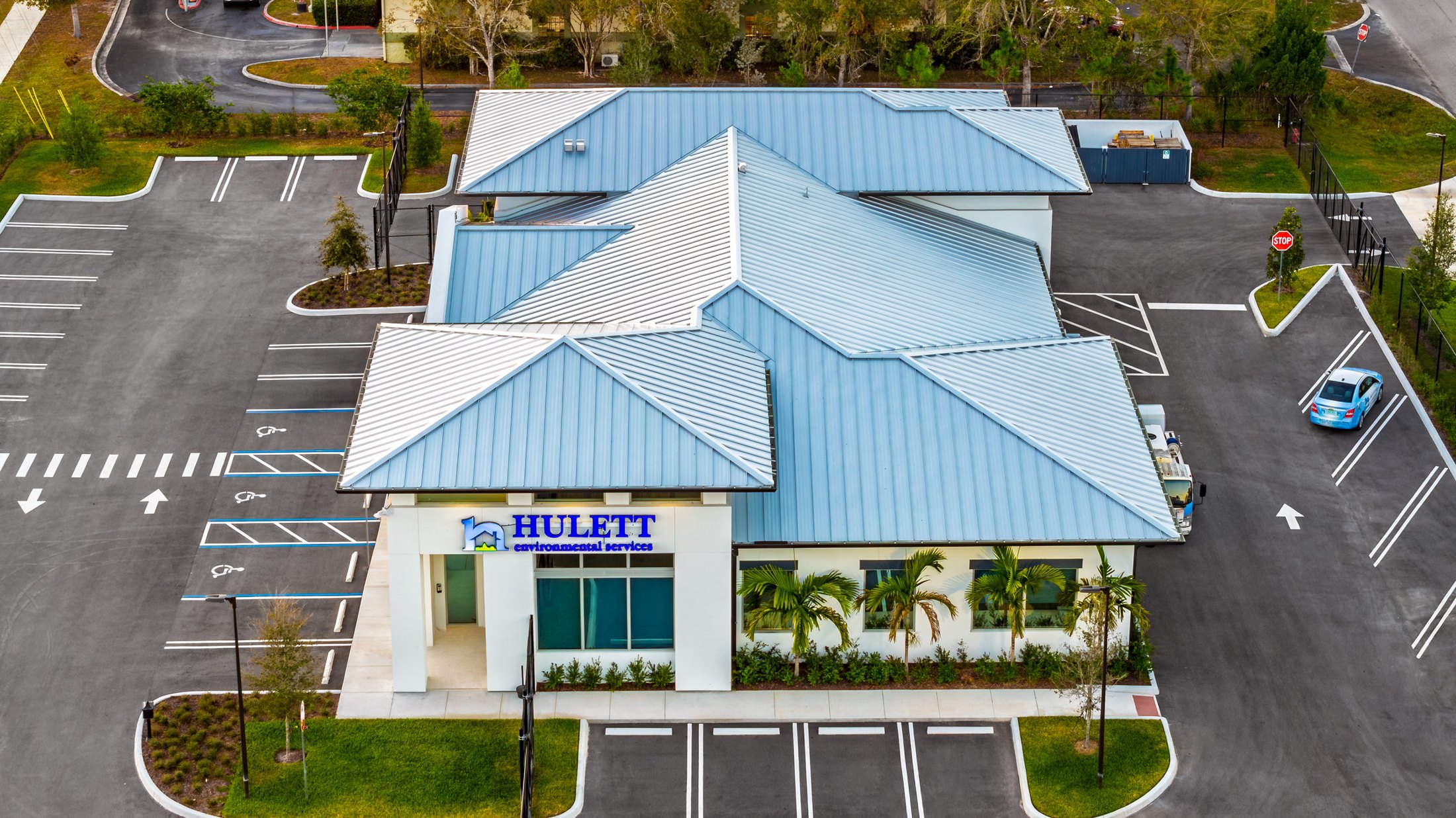 Hulett Environmental aerial — three-quarter view from above the blue metal hipped roof, showing the complete envelope and the relationship between the two-story entry and the wing