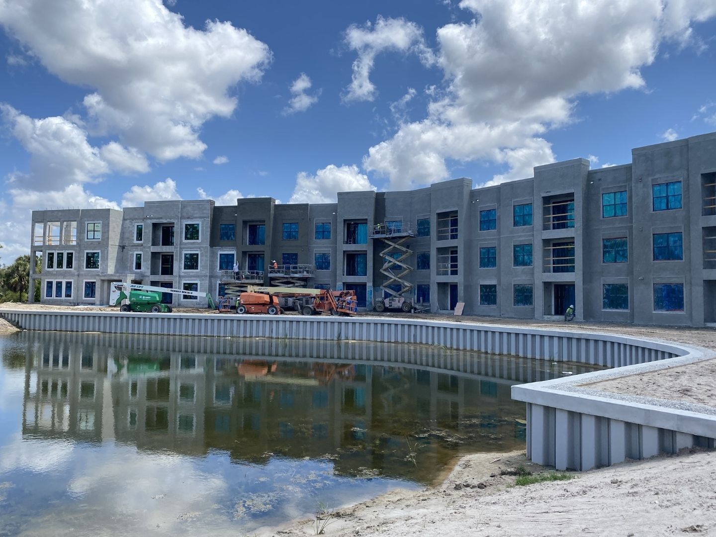 Imperial Crossings main apartment building during construction Bonita Springs — three-story multifamily with PGT impact windows, boom lifts and scissor lifts on site, ACG glazing contractor