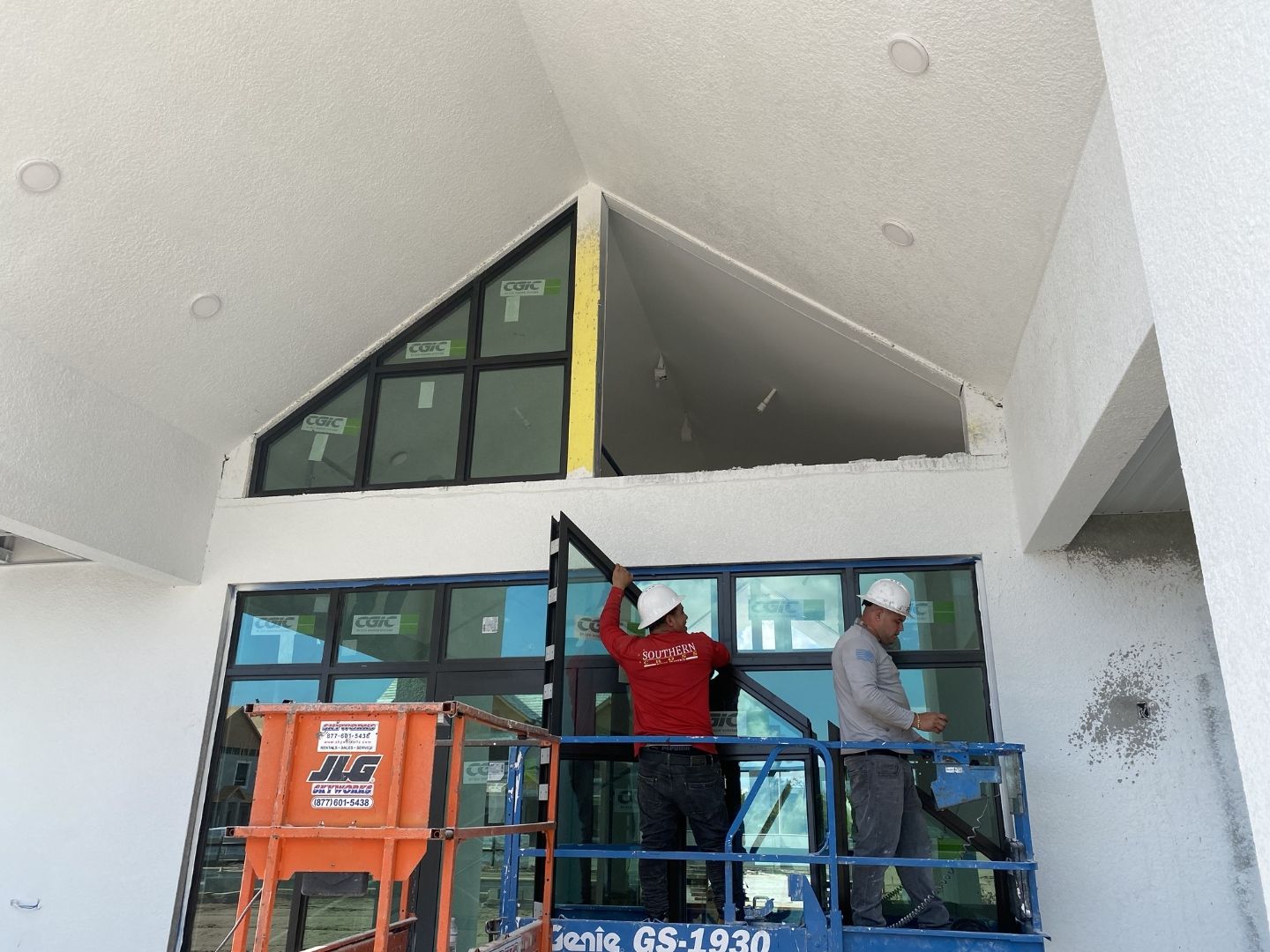 ACG glazing crew installing clubhouse entry storefront at Imperial Crossings Bonita Springs — triangular gabled glass system on scissor lift, ESWindows commercial storefront