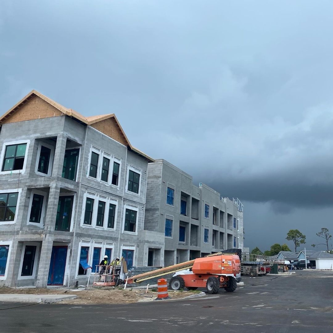 ACG crew installing PGT impact windows on three-story apartment building at Imperial Crossings Bonita Springs — boom lift active, dramatic Florida storm clouds approaching