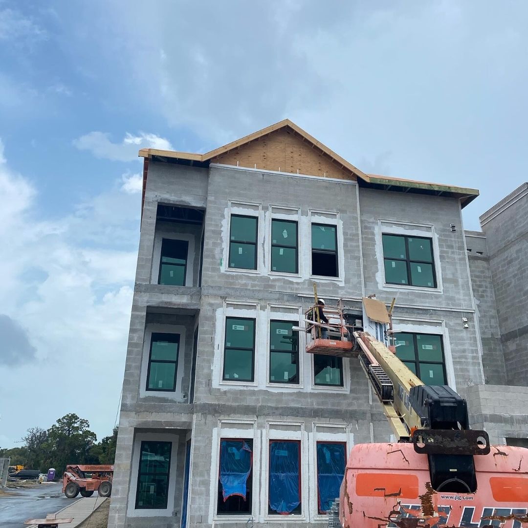 Close-up of PGT impact window installation at Imperial Crossings Bonita Springs — three floors of hurricane-rated windows being installed by ACG glazing crew on boom lift