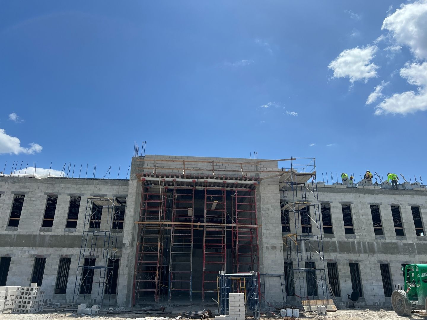 KLUS Lighting Vero Beach earlier in construction — CMU block facade with commercial window openings framed and crew on parapet preparing for ESWindows storefront installation, Proctor Construction