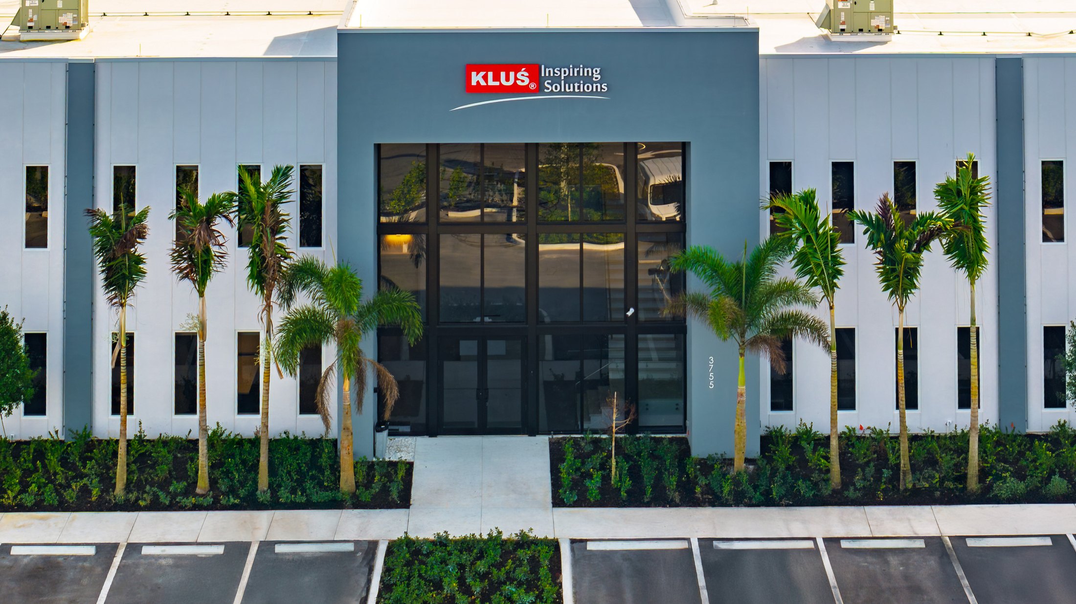 KLUS Lighting Vero Beach entrance tower — close view of the two-story ESWindows storefront with KLUS Inspiring Solutions signage above, framed by palms