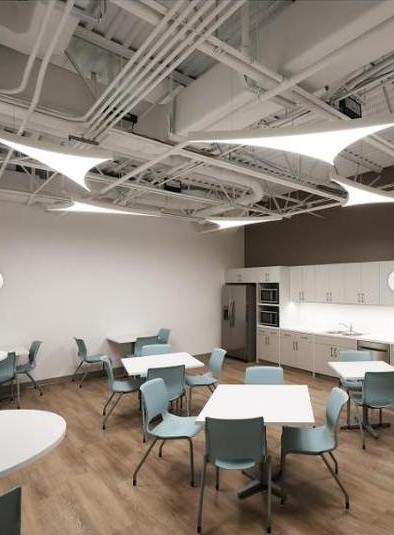 KLUS Lighting Vero Beach break room — KLUS sculptural triangular LED ceiling fixtures over dining tables with teal chairs, exposed structural ceiling, kitchen casework along the back wall