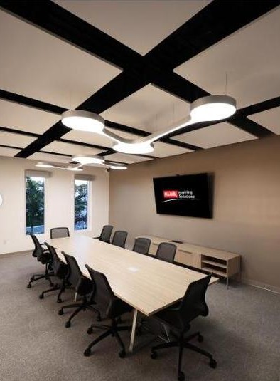 KLUS Lighting Vero Beach conference room — grid-coffered black ceiling with circular pendant LED fixtures over a long conference table, KLUS Inspiring Solutions branded display on the wall