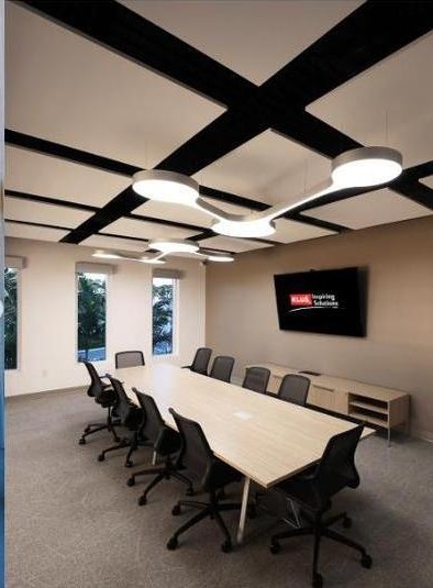 KLUS Lighting Vero Beach conference room wide angle — full length of the conference table with LED ceiling pendants, punched windows along the side wall, KLUS Inspiring Solutions branded display