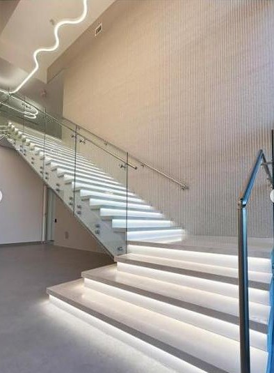 KLUS Lighting Vero Beach illuminated staircase — LED strip lighting under each tread, glass railing on stainless posts, custom wavy LED accent feature on the wall above