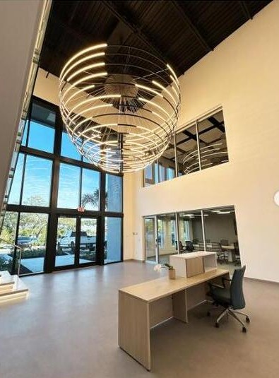 KLUS Lighting Vero Beach finished lobby — dramatic circular sculptural KLUS LED chandelier suspended in a double-height entry, looking out through the two-story ESWindows storefront installed by ACG, reception desk in foreground