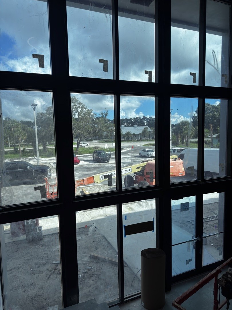 KLUS Lighting interior — view from inside the showroom looking out through the freshly installed two-story entry storefront, parking lot and ACG service vehicles visible beyond the glass