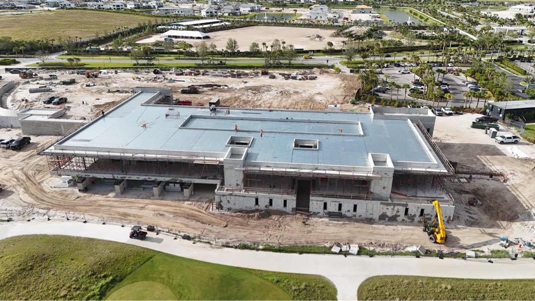 Panther National Clubhouse construction — aerial view of the two-story structure with deck-level slab poured and glazing openings ready for Euro-Wall DirectSet, multi-slide, Vistafold, and pivot installation